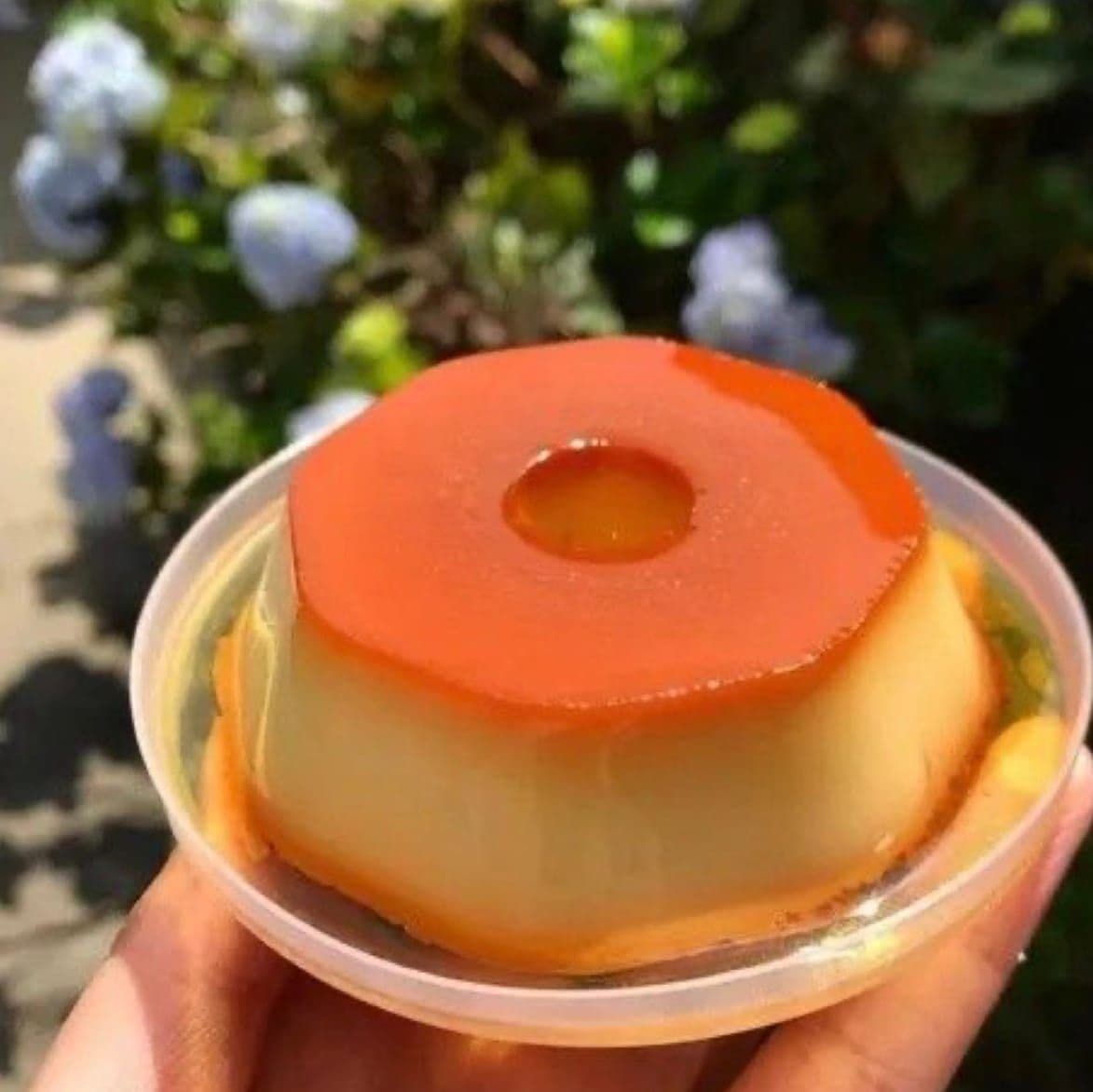 Pudim individual com calda de caramelo em um potinho, segurado ao ar livre
