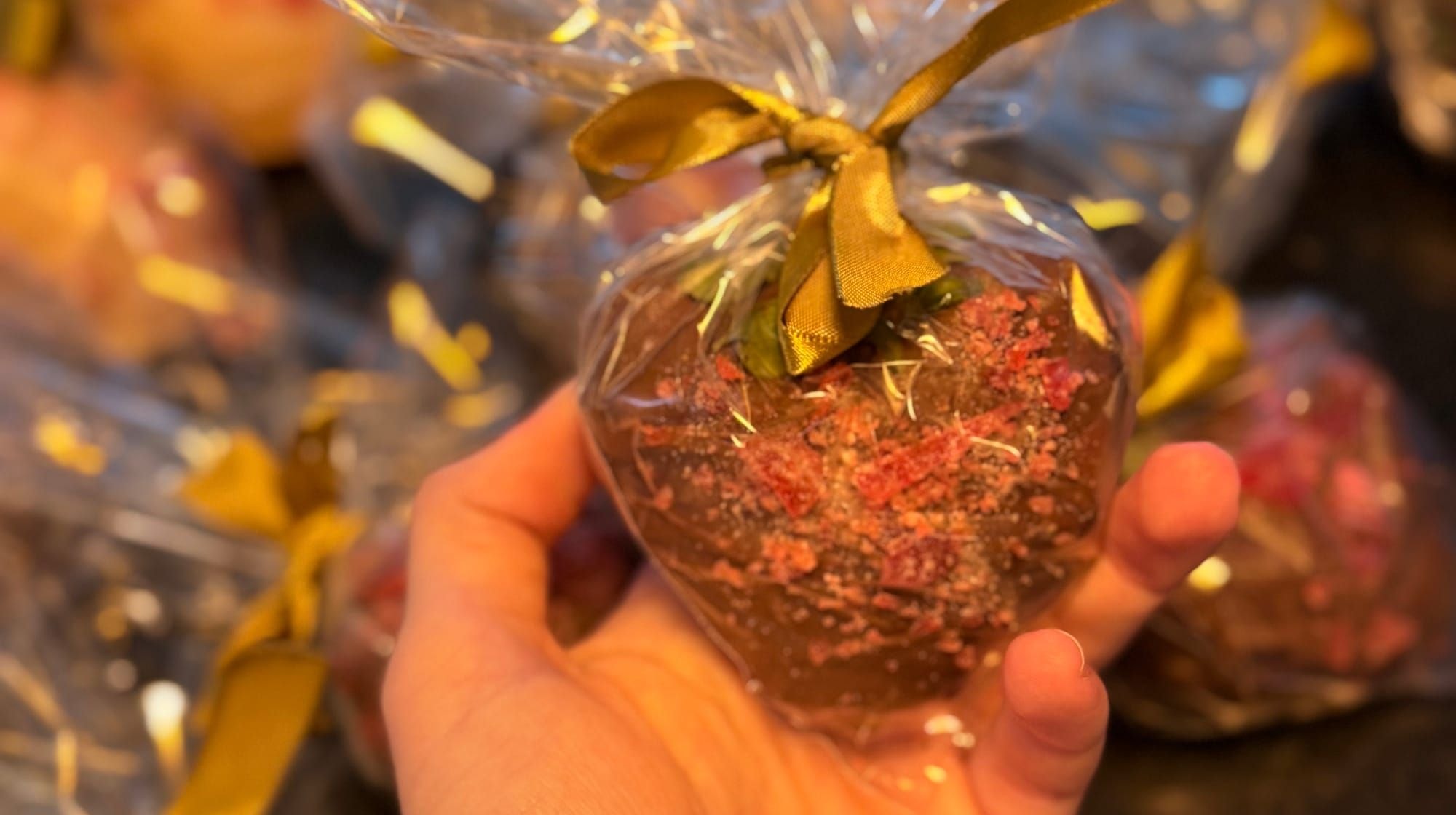 Mão segurando um morango cravejado de brigadeiro embalado com laço dourado